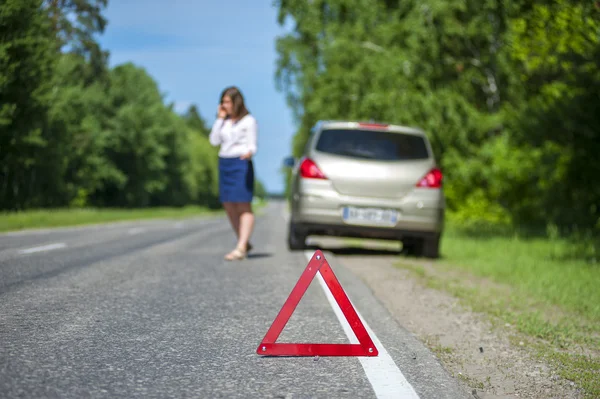 Red triangle warning sign and woman near broken car