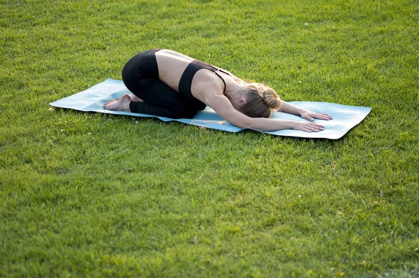 Slim woman in sportswear doing yoga on green grass