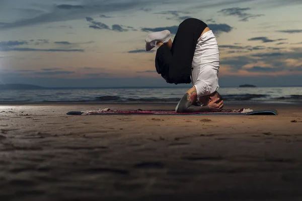 Flexible yoga man doing head stand on the beach