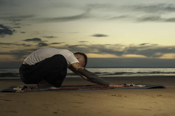 Young tattoo man practicing yoga pose on the beach