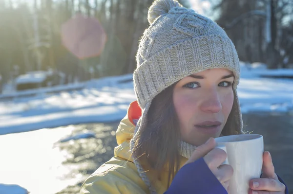 Woman holds white cup of coffee. Sunny winter day. Girl drinking coffee  next to the river.