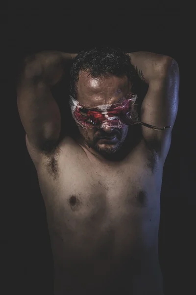 Naked man with blindfold soaked in blood