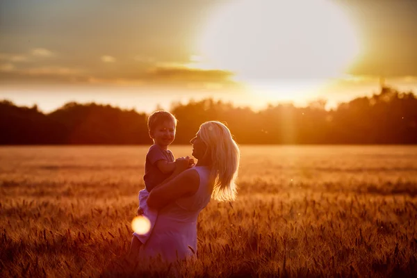 Mom and son having fun by the lake, field outdoors enjoying nature. Silhouettes on sunny sky. Warm filter and film effect