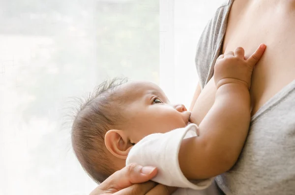 Mother breastfeeding her newborn baby beside window