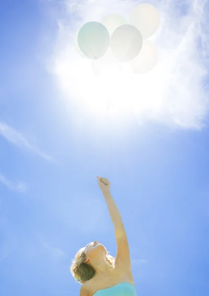 Young girl holding balloons on a background of the sun
