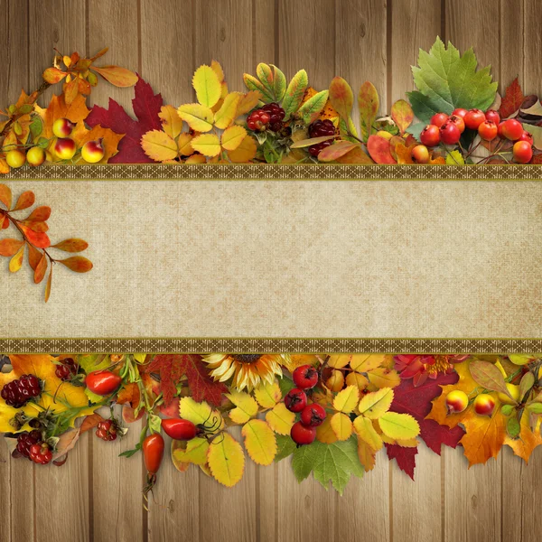 Border of autumn leaves and berries on a wooden background