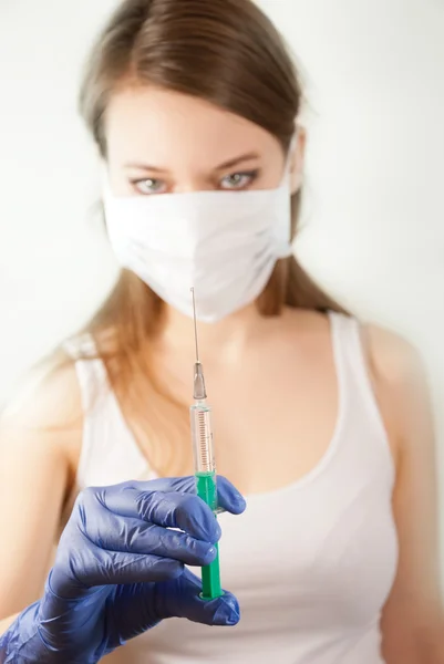 A young beautiful woman wearing a mask and gloves and holding a syringe