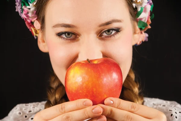 A young beautiful woman wearing a traditional Polish folk costume with an apple on a black background