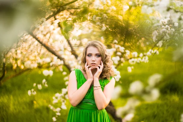 Beautiful young blond woman standing beside a blossoming Apple tree