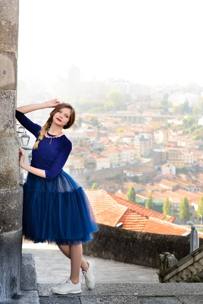 Young elegant woman in blue long flying dress posing at stairway against old city building