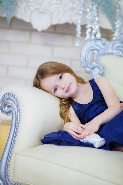 Little girl in an elegant dress sitting by the fireplace