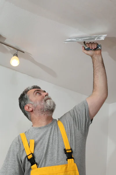 Home renovation, worker repairing plaster at ceiling