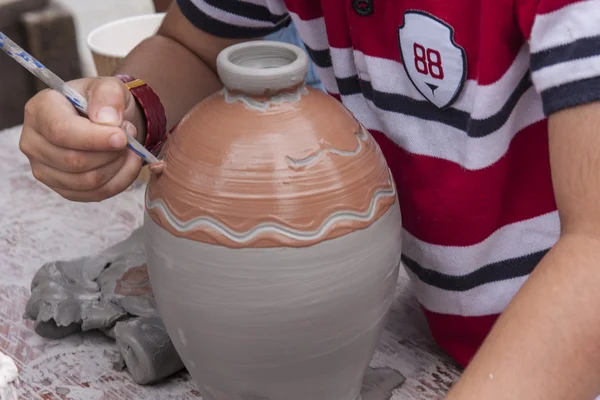 A young boy decorates a wet clay pot