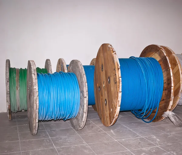 Big industrial wooden spools of blue and green wires on grey flo