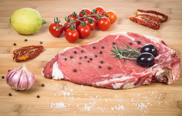 Raw fiorentina steak with spices and vegetables on a wooden tabl