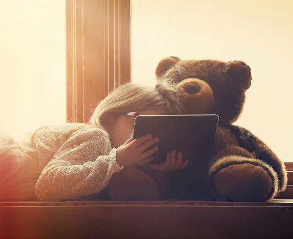 Casual Child Holding Tablet with Teddy Bear at Home