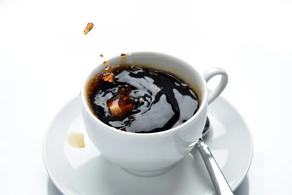 Coffee splashing in cup, sugar cube dropped in, white background