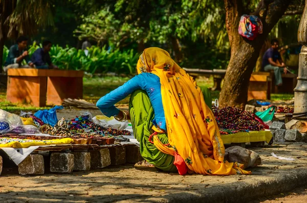 Indian woman in colorful sari sells souvenirs, bangles and cheap jewelry at street market place.
