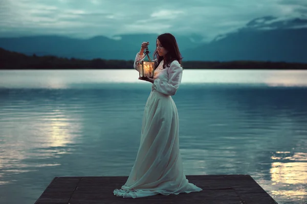 Sad bride on lake pier with lantern