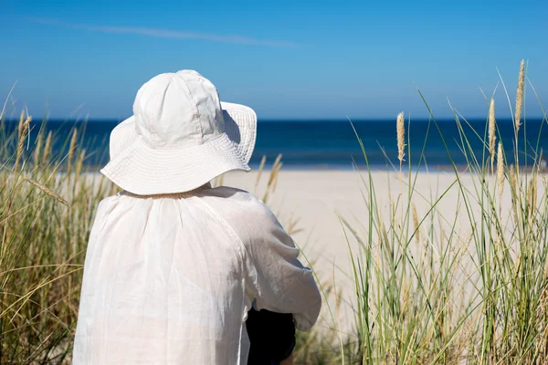 Woman sitting on sand dune and looking at sea