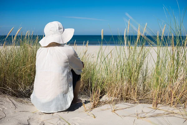 Woman sitting on sand dune and looking at sea