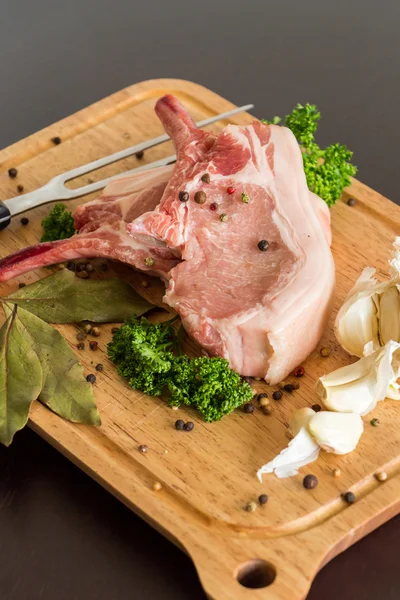 Preparing pork cutlets with bay leaf, garlic cloves, peppercorns and parsley displayed on a wooden chopping board