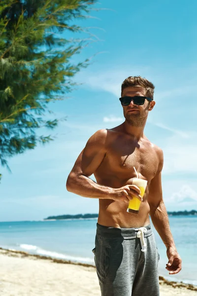 Man With Muscular Body Drinking Healthy Drink On Beach. Summer
