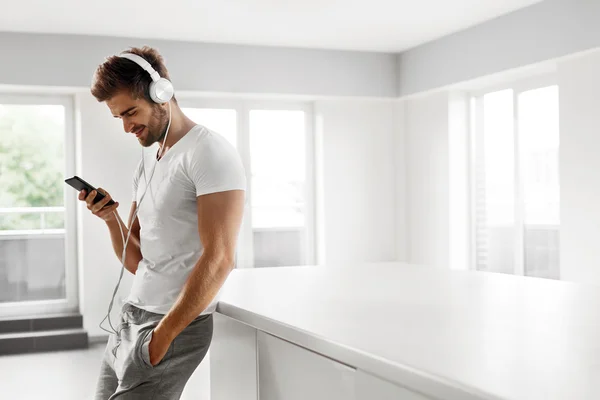 Man Listening To Music In Headphones Using Mobile Phone Indoors