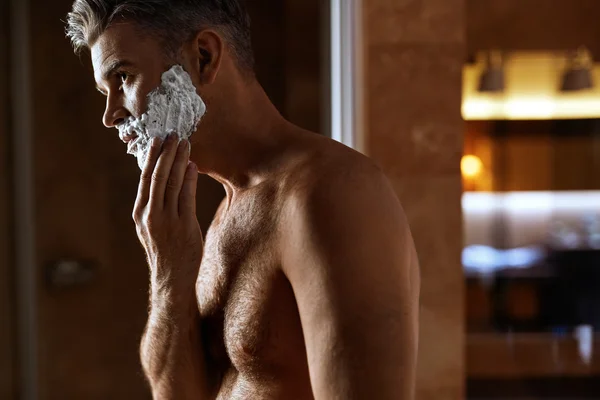 Man Using Shaving Cream On Face In Bathroom. Men Skin Care