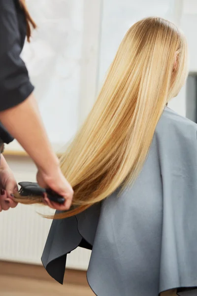 Hairdresser combing long blonde hair