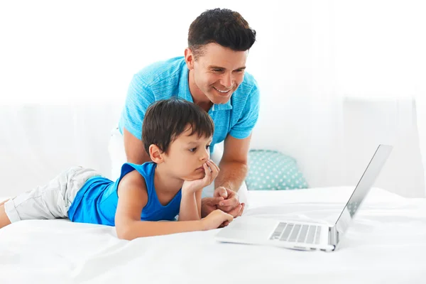 Father and son using notebook in bedroom