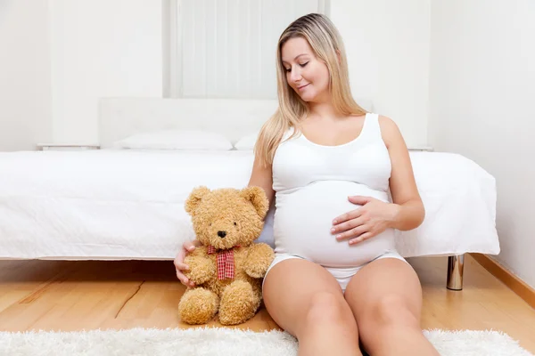 Young pregnant woman sitting on the floor with a teddy bear