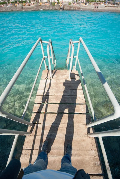 Old vintage metal wooden stairs leading to blue turquoise sea water from beach. Beautiful summer day. Swimming pool with grunge retro stairs on the ocean coast. Top POV, Point of view shot