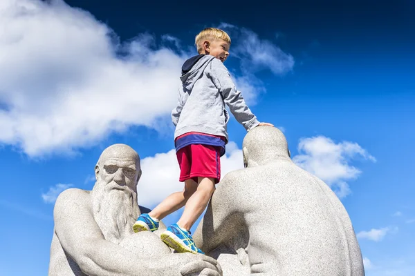 Oslo, Norway - August 11, 2016: Smiling boy over sculpture in Vigeland Park, the world\'s largest sculpture park made by a single artist, and one of Norway\'s most popular tourist attractions.