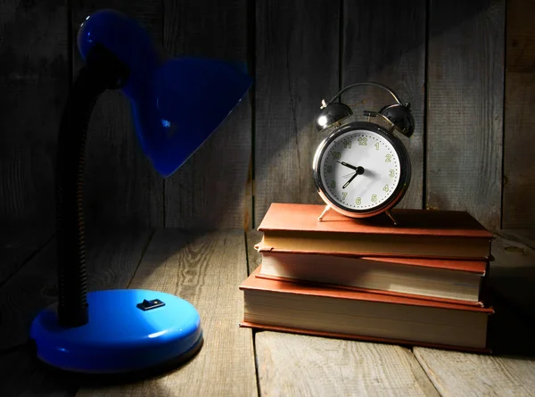 Alarm clock and books. On wooden background.