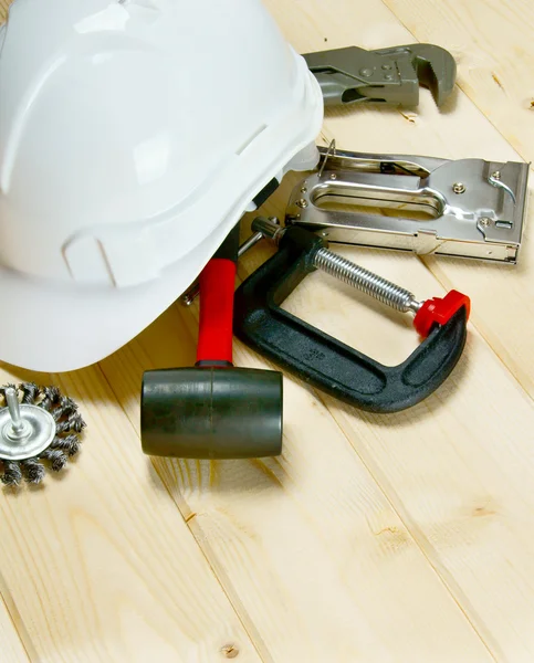 Helmet, clamp, stapler and other tools on wooden background.