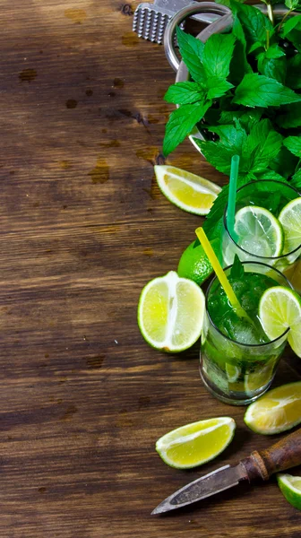 The ingredients for the cocktail- limes, rum, mint leaves, ice cubes on wooden table.