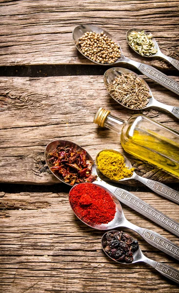 Fragrant spices in spoons with a bottle of olive oil.