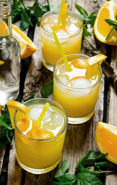 Three cocktails from fresh oranges with ice and mint leaves on wooden background