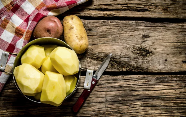 Peeled potatoes in an old pan with knife on wooden table . Free space for text.