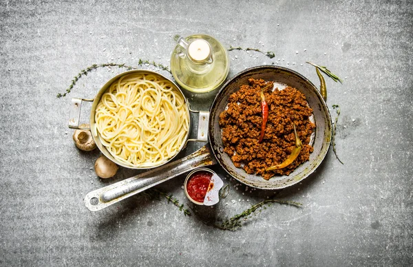 Spaghetti in pan and ground beef in a pan with herbs and olive oil.