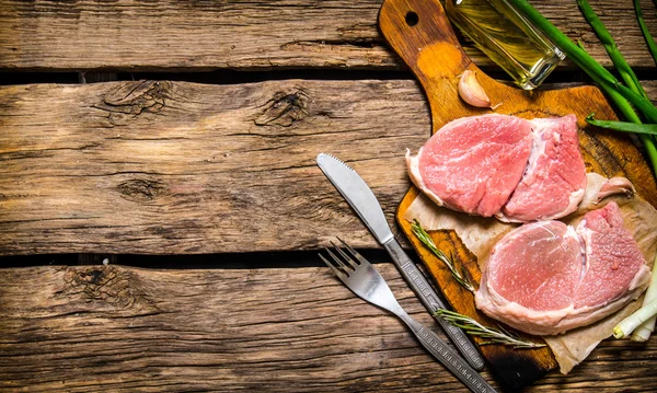 Fresh raw steaks on the old Board with the onion and garlic.