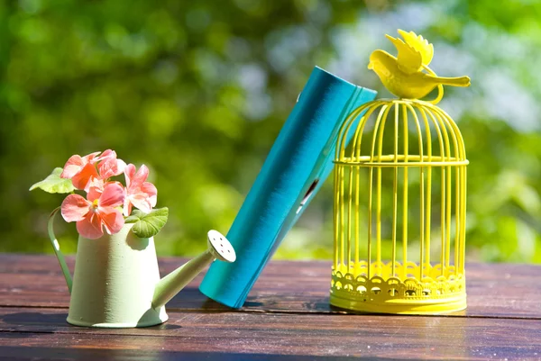 Decorative bird cage, book and flowers in can