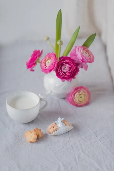 A vase of flowers and a cup with milk and cookies