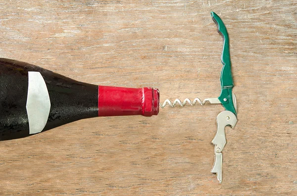 Red wine bottle with opener on wood background