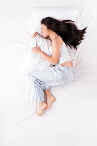 Woman sleeping in fetal position with pillow