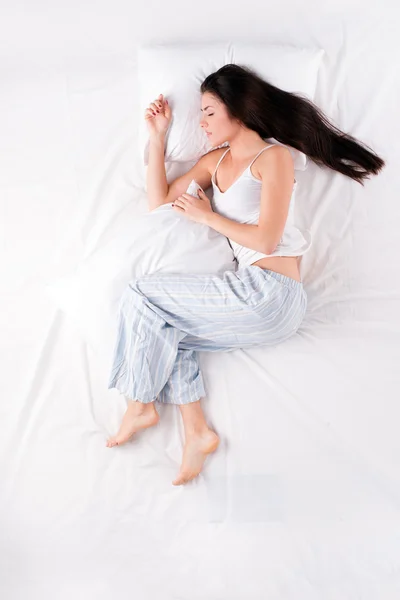 Woman sleeping in open fetal position with pillow
