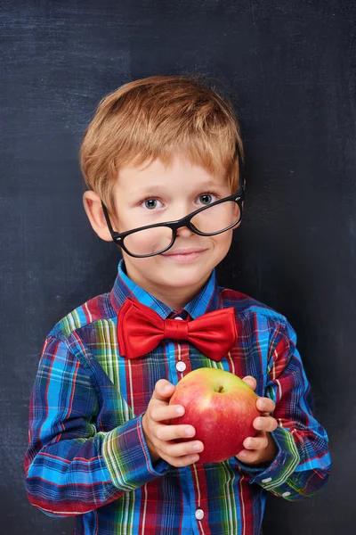 Mixed-up ginger primary school age boy holding red apple