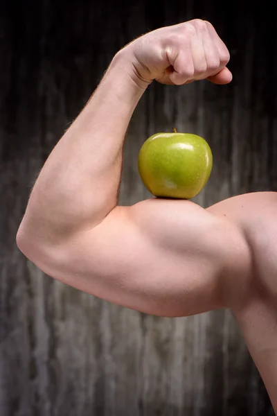 Close up of sporty man demonstrating biceps with apple