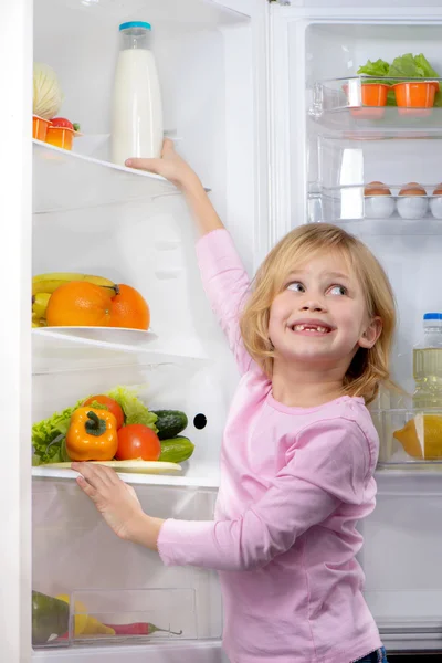 Funny smiling girl trying to pick food from fridge